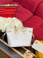 A Louis Vuitton Neverfull tote bag in the classic Monogram canvas, styled on a Louis Vuitton suitcase next to a red sofa and white roses.