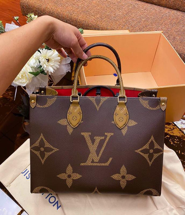 A Louis Vuitton monogram handbag in dark brown coated canvas with tan leather handles and trim, held by a hand over a beige dust bag with its signature orange box in the background.