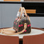 A Louis Vuitton monogram dome handbag with pink cherry embellishments, displayed on a brown leather circular table against a gray and black background.