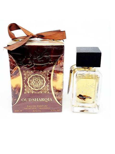 Oud Sharqia Eau de Parfum bottle with a black cap next to its brown and gold patterned box tied with a brown ribbon, on a white background.
