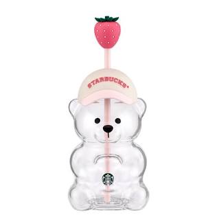 A clear Starbucks bear-shaped cup with a pink straw, topped with a pink strawberry cap featuring the Starbucks logo.