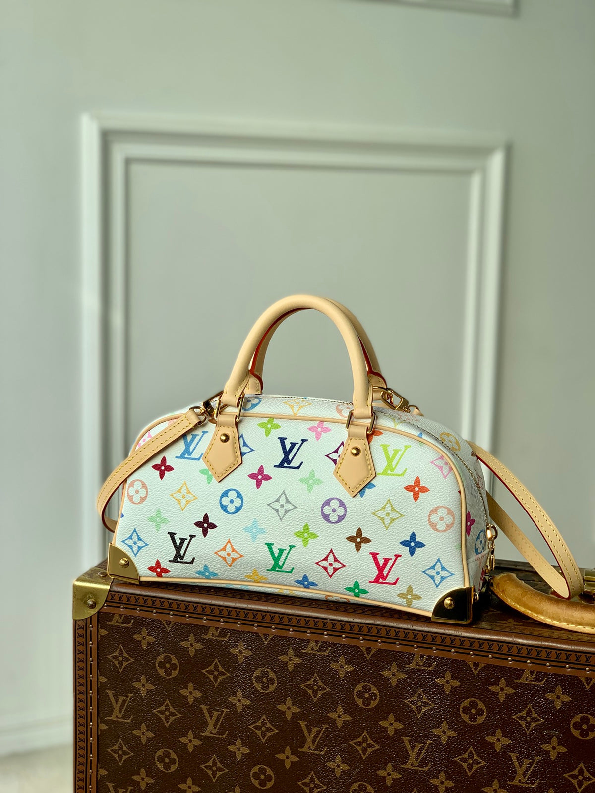 Designer handbag with multicolor monogram pattern on a matching box against a neutral background