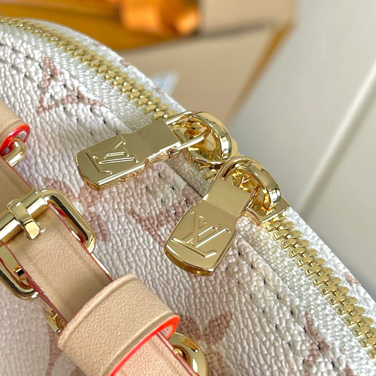 Close-up of a Louis Vuitton handbag featuring a cream and pink monogram canvas, gold-tone hardware, and a beige leather strap with gold-tone zipper pulls engraved with the LV logo.